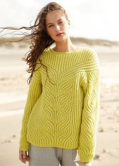 a woman standing on the beach wearing a yellow sweater