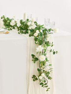 white flowers and greenery are arranged on the table