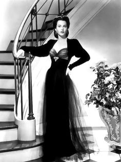 an old photo of a woman in a long dress standing on the stairs with her hands on her hips