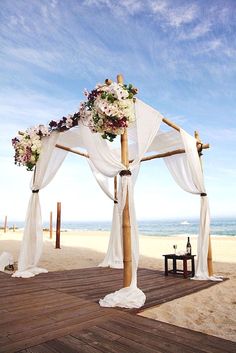 an outdoor wedding setup on the beach with white draping and floral arrangements in front of the ocean