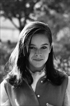 a black and white photo of a woman with long hair wearing a vest, smiling at the camera