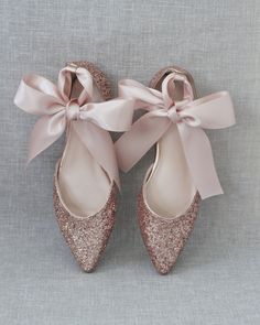 a pair of pink glitter shoes with a bow on the front and side, against a gray background