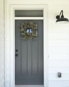 a gray front door with a wreath hanging on it's side and a black light next to it