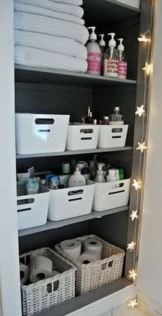 an organized bathroom closet with white baskets and lights on the shelves, all filled with personal care items