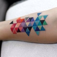 a person with a colorful tattoo on their arm that has triangles in different colors and shapes