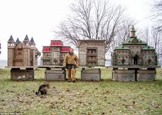 a man is standing in front of some wooden buildings and a cat on the grass