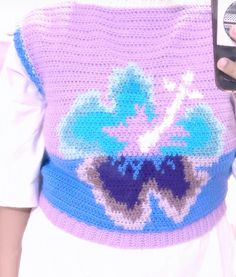 a close up of a person holding a cell phone and wearing a crocheted sweater