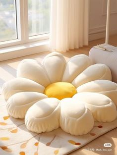 a large flower shaped pillow sitting on top of a rug in front of a window