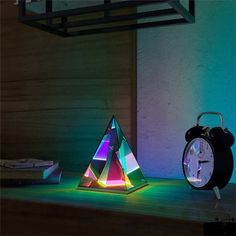 an alarm clock sitting on top of a wooden table next to a neon light pyramid