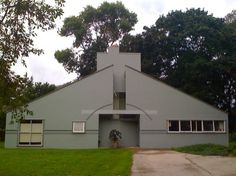 a large gray building sitting in the middle of a lush green field next to trees