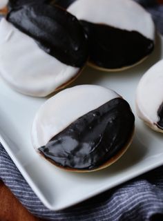 four cookies with black and white frosting on a square plate, sitting on a striped cloth