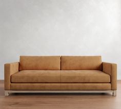 a tan couch sitting on top of a hard wood floor next to a white wall