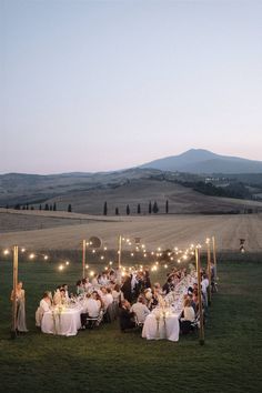 a group of people sitting around a dinner table in the middle of an open field