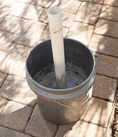 a white tube sticking out of the top of a metal bucket on a brick walkway