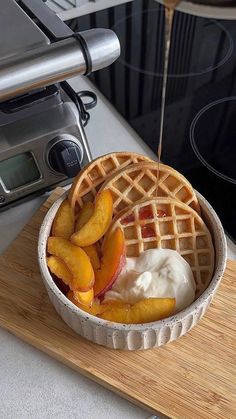 a waffle topped with peaches and ice cream on a cutting board next to an oven