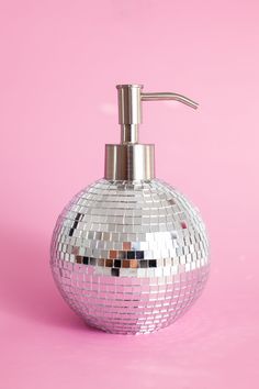 a silver soap dispenser sitting on top of a pink surface with disco balls