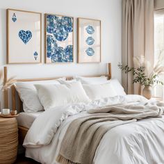 a bed with white sheets and pillows in a bedroom next to two paintings on the wall