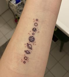 a small tattoo on the arm of a woman with planets and stars around it in black ink