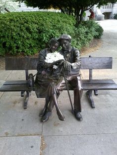 a bronze statue of two people sitting on a bench with flowers in their hands,