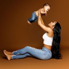 a woman holding a baby up to her face while sitting on the floor in front of a brown background