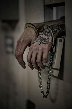 a man's hand holding onto a chain with tattoos on his arm and wrist