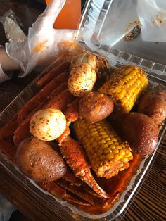 a plastic container filled with cooked corn on the cob and hot dog buns