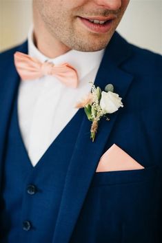 a man wearing a blue suit with a pink bow tie and white flower in his lapel