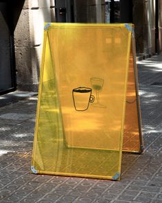 a yellow sign sitting on the side of a street next to a sidewalk with a coffee cup drawn on it