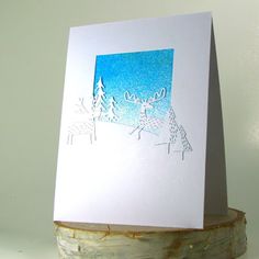 a card with some deer on it sitting on top of a piece of driftwood