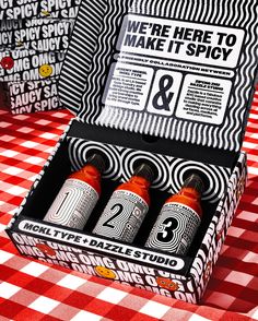 two hot sauce bottles in a box on a table with red and white checkered cloth