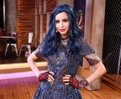 a woman with blue hair and gloves standing on a wooden floor in front of a tv screen