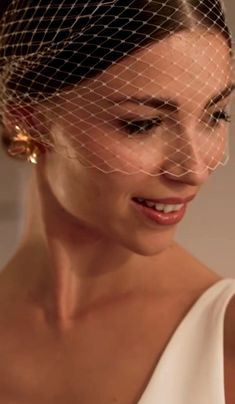 a woman in a white dress wearing a birdcage veil on her head and smiling at the camera