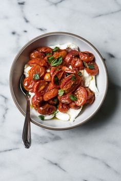 a bowl filled with tomatoes and cream on top of a marble counter next to a spoon