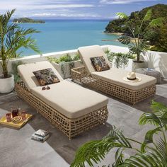 two wicker chaise lounges on a patio overlooking the ocean and tropical trees