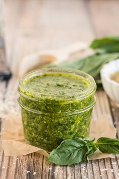 a jar filled with green pesto next to two small bowls of pesto sauce