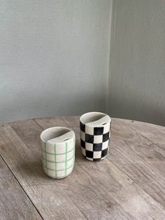 two checkered cups sitting on top of a wooden table next to eachother