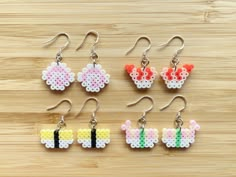 four pairs of cross stitch earrings with bows and ears on them, sitting on a wooden surface