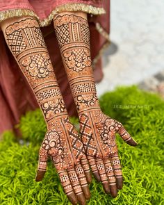 the hands and feet of a woman with henna tattoos on their arms, in front of some green grass