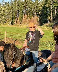 three people are sitting on horses in a fenced area and one person is holding the horse's bridle