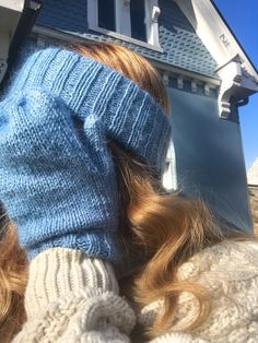 a woman wearing a blue knitted mitt in front of a house with her hands on her head