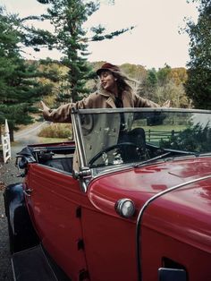 a man standing in the back of an old red car with his arms out wide