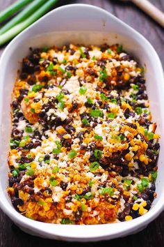 a casserole dish filled with black beans, corn and green onions on a wooden table