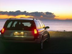 a car is parked on the side of the road by the water at sunset with clouds in the sky