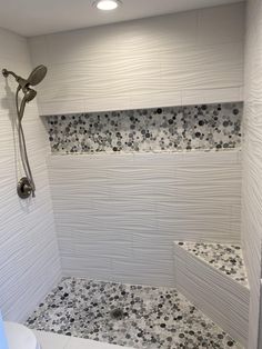 a white tiled shower with black and gray flowers on the wall next to the bathtub