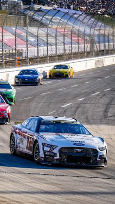 two cars racing on a race track with spectators in the stands watching from behind them