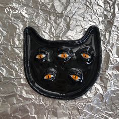 a black cat shaped object with orange eyes on aluminum foil covered surface in the shape of a face