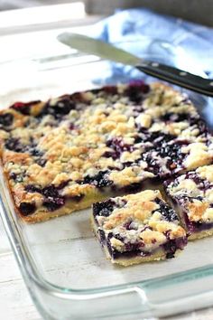 blueberry crumb bars sitting on top of a glass tray next to a knife