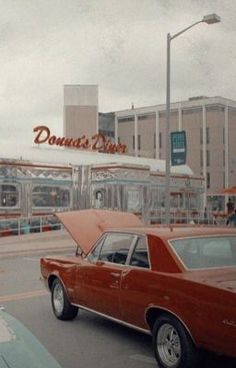 an old red car parked in front of a donut shop