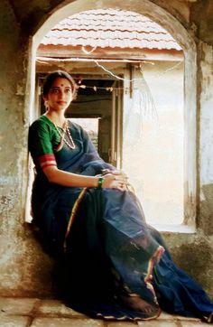 a woman sitting on the ledge of a window sill wearing a green and blue sari