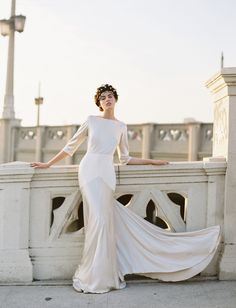 a woman in a white dress standing on a bridge with her hands on her hips